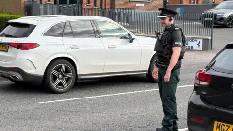 Pacemaker A police man stands on the road ready to check a car. 