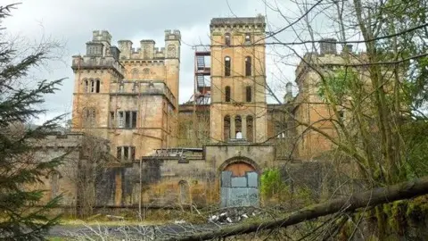 The hospital is a Scottish Baronial-style property with square-shaped towers and turrets and long narrow windows. The light brown coloured building is falling into ruin.