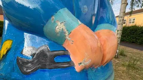 A blue rat sculpture in Brough. Parts of the sculpture appear to have been chipped off.