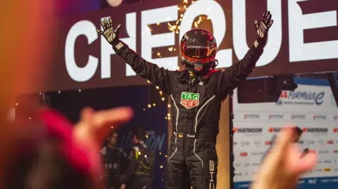 Craig Evans Pascal Wehrlein wearing a black racing suit and a black and red helmet holding his arms aloft as he celebrates a victory