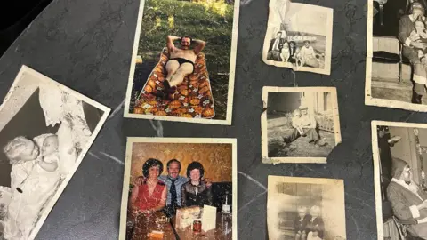 William Lindsay Family photos are spread out across a kitchen table, showing black and white images of children and families as well as a few colour images.