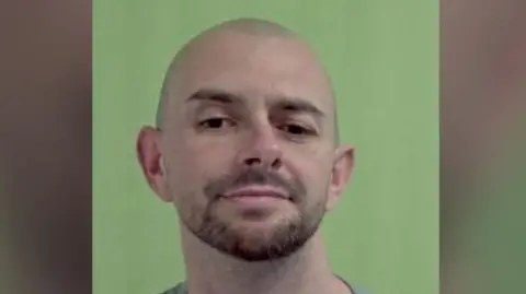 IOM POLICE Jamie Smith, a man who is bald with brown stubble, in front of a green background.