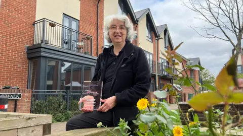 BBC Frances Halstead sat among the community garden, in front of new build houses