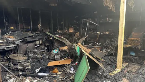 BBC An office building completely gutted and destroyed by fire. There are charred, blackened and broken pieces of furniture and items strewn around, with the roof exposed and blown out windows