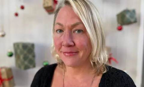 A woman with blonde hair looks at the camera with a serious face