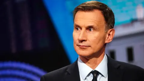 Jeremy Hunt looks away from camera wearing a suit and tie during a TV interview in April