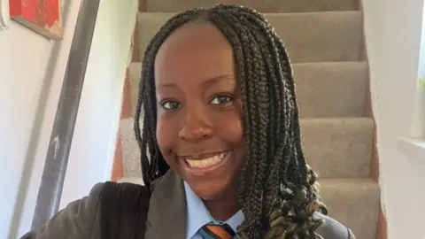 Supplied by family Vivica smiling at the camera while wearing a school uniform of a grey blazer, a blue shirt and a orange and blue striped tie. Her long black hair is braided.