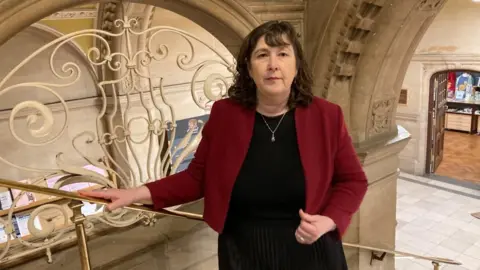 A woman is standing on an old staircase. She is wearing a red jacket and a black dress. 
