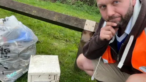 Sam Laywood A man in high-vis kneeling by a safe and a bin bag