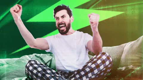 BBC A man dressed in black and white pyjamas sits on a couch and cheers on a football match. Green World Cup branding is in the background. 