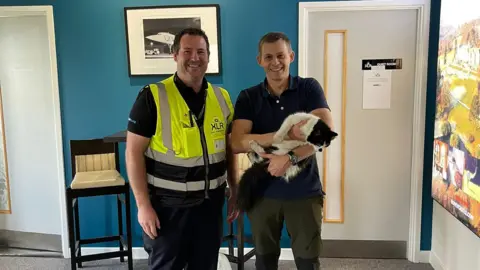 Exeter Airport Ted the cat with Exeter airport employee Alex Stephenson and his owner Rich Fleming