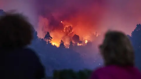 EPA Duas pessoas em primeiro plano ficam de costas para a câmera e assistem a um incêndio florestal que se espalha por uma floresta em Silvares, Portugal, na sexta-feira.