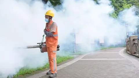 Getty image of sanitation workers wearing yellow helmet and orange uniform spray to prevent spread of Donggua in Guangdong on August 3