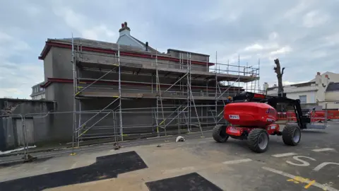 Government of Jersey Steel strapping is positioned from the road up two storeys of a building.
A red piece of machinery used for lifting equipment is positioned to the right.