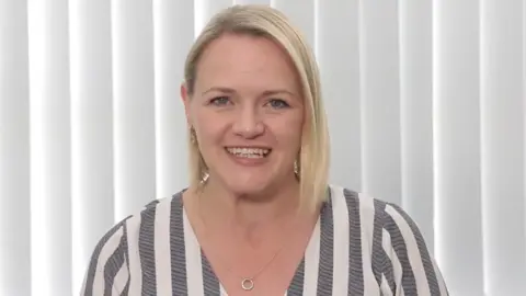 Fiona Graham Dr Graham is smiling at the camera. She has  shoulder length blonde hair, with blue eyes and is smiling at the camera. She is wearing a pin-striped grey and white top.
