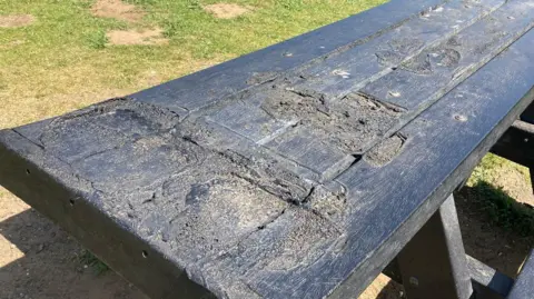 A black picnic bench with several large melted patches on top