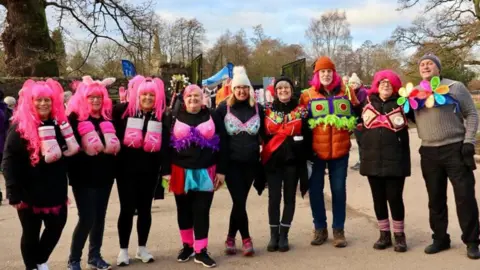 Bradgate Rotary Club Walkers standing in a line wearing decorated bras on top of their clothes and some with pink wigs at Bradgate Park in Leicestershire.
