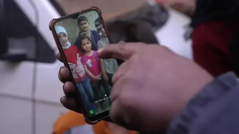 Tawfiq Diam points to a picture of his four children, on his mobile phone