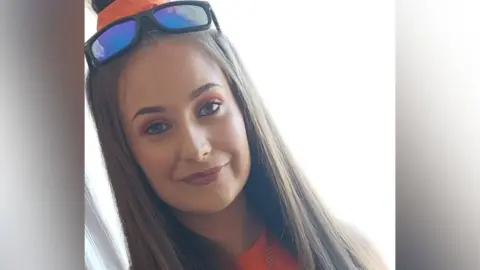 Family handout Chloe Mitchell is smiling in the picture. She has part of her hair tied up in a high bun using an orange scrunchie, while the rest is straightened. She is wearing makeup and an orange top. She also has sunglasses on her head.