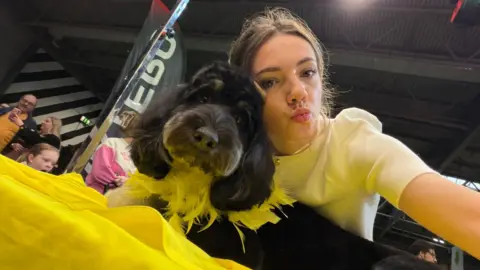 Mia Blackburn The same woman and dog, looking down at the camera as she takes a selfie and pouts at the camera.