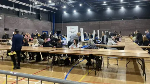 Bethan Rush/BBC People sit at tables waiting to count votes
