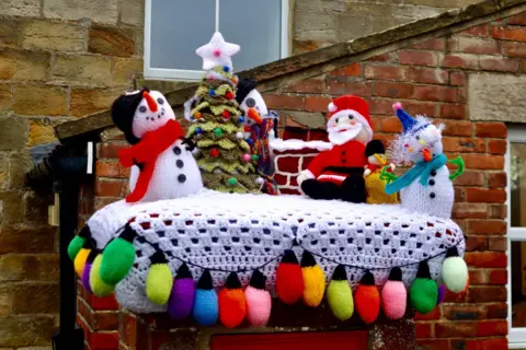 BBC WEATHER WATCHERS / ALASTAIR A knitted scene depicts a three snowmen and Santa gathered around a Christmas tree.