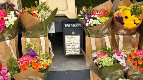 Jamie Kelly Bouquets surrounds a box that reads 'PAY HERE!'. Stuck to it is a list of ways you can pay. 