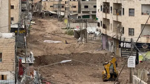 A street with part of the dirt road dug up by a digger
