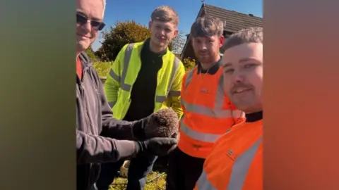 Yorkshire Water Three men in hi-vis and one in a grey jacket who is holding a hedgehog which has just been rescued. 