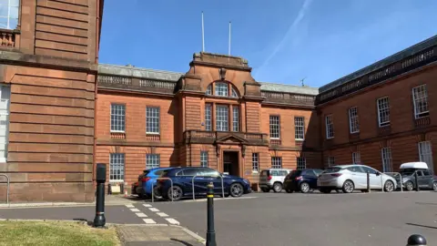 The sandstone headquarters of Dumfries and Galloway Council - an imposing facade with a number of cars parked in front of it