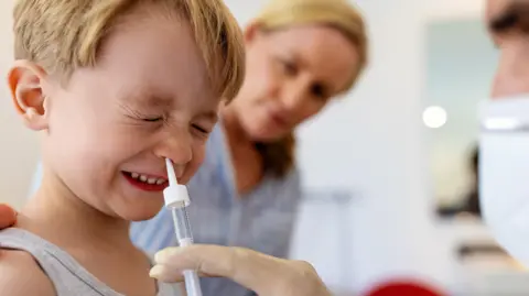 A child being given a nasal vaccination by a doctor as his mother looks on.