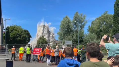 BBC People hold their camera phones up as the towers come down