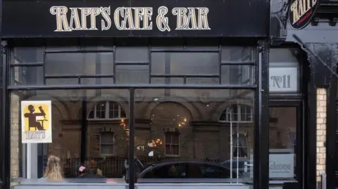 The exterior of Rapp's Cafe & Bar. It has a large glass window while the frames and walls are painted black with a logo in gold above.