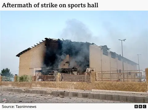 An image showing the aftermath of the strike on the sports hall. It clearly shows damage to the wall as smoke rises from the site.