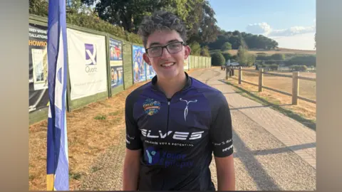 Sarah Brinicombe/BBC Zac after the challenge in Reigate, Surrey. Zac is at the finish line, and is wearing a purple cycling top.