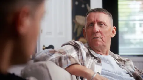  Kusini Productions Pete wearing a white T-shirt and checked shirt