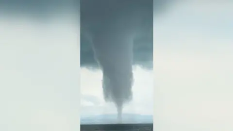 A waterspout seen over water with huge clouds forming above.