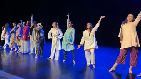 Jon Wright/BBC A line of women wearing colourful clothing line up on a stage