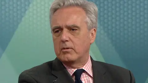 Conservative MP Mark Garnier, a man with grey hair, wearing a pink- and white-check shirt with a blue tie under a dark jacket.