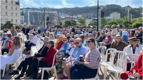 BBC Last year's Liberation Day celebrations in Jersey. Islanders are sat in Liberation Square.