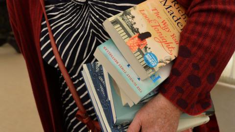 An older woman holding a pile of books