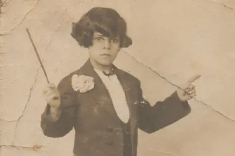 Herbert King A black and white photo of a young Herbert King wearing a formal jacket and shirt. He is holding a music baton