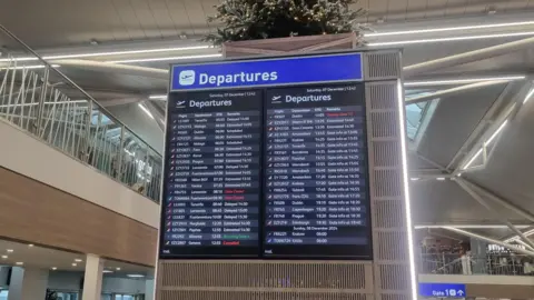 A departure board inside Bristol Airport, detailing flights due to take off, flights which are delayed and which gates are open for passengers.