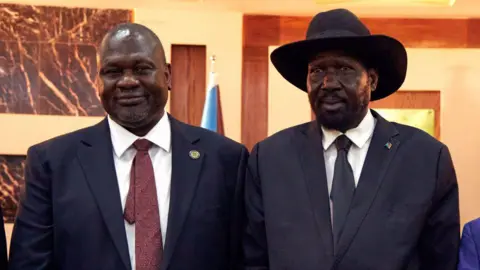 AFP First Vice President Riek Machar wearing a dark suit and red tie (L) and President Salva Kiir wearing a dark suit and a dark tie with a black widebrim hat (R).