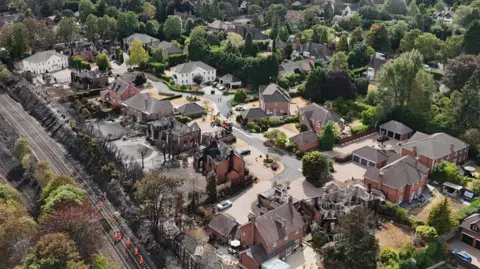 An aerial view of the devastation that wildfires have taken on an area of Stourbridge. Several houses are blackened or destroyed, with a field behind the houses completely black.