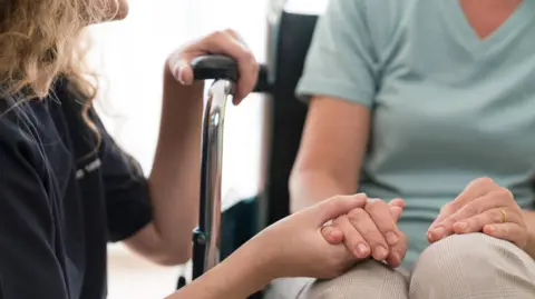 Stock image of a carer holding the hand of someone in a wheelchair