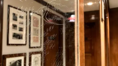Kit Taylor/BBC A mirror with names and messages carved into it from a side view. 