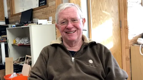 Ian McCathie pictured smiling at the camera wearing a dark green fleece. He has short grey hair and glasses.