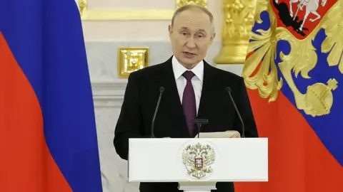 Vladimir Putin stands at a lecturn wearing a suit and purple tie with the Russian flag behind him to the left, in Moscow on 5 November (file photo)