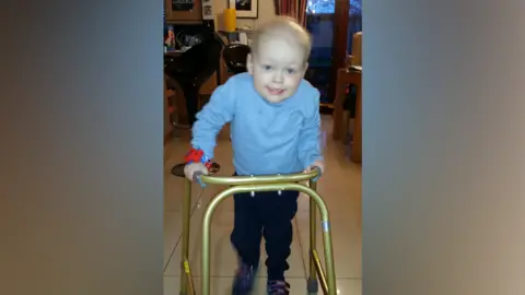 Family Carter as a young child, about five, using a frame to walk 